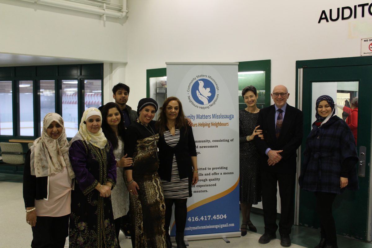Neighbours gathered at a Community Matters Mississauga community evening, standing together beside the organization's vision and mission banner
